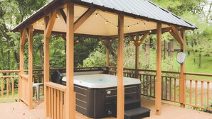 Um gazebo de madeira com banheira de hidromassagem, rodeado por um deck de madeira e um telhado de metal.
