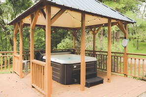 Eine hölzerne Laube mit Whirlpool, umgeben von einer Holzterrasse und einem Metalldach.