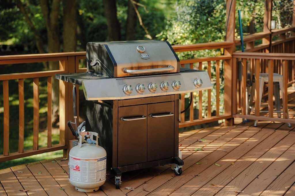 Un barbecue portatif avec une bouteille de gaz, installé sur une terrasse en bois.