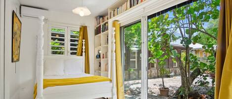 Une chambre à coucher avec un lit, une bibliothèque, une fenêtre avec des rideaux et une vue sur l’extérieur.