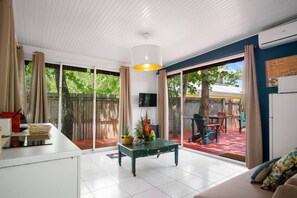 A spacious living area with a sliding glass door leading to an outdoor patio, a dining table with chairs, and a sofa. - Les Beaux Arts Bungalow (Le Diamant)
