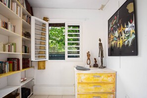 A room with a bookshelf, a window with blinds, a dresser, and a painting on the wall. - Les Beaux Arts Bungalow (Le Diamant)