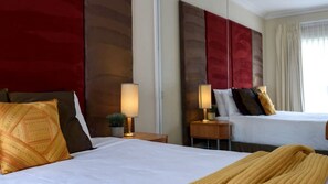 Een hotelkamer met twee bedden, elk voorzien van een witte spreidek en meerdere kussens. Er staan nachtkastjes met lampen en een kleine plant op een van de tafels.
