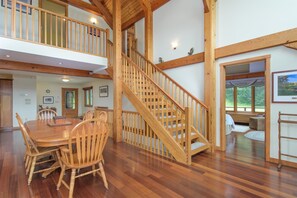 Dining area beside an exposed wood staircase leading to an upper loft. - Ludlow Treasure | Okemo, Hot Tub, Game Room, Views (Ludlow)