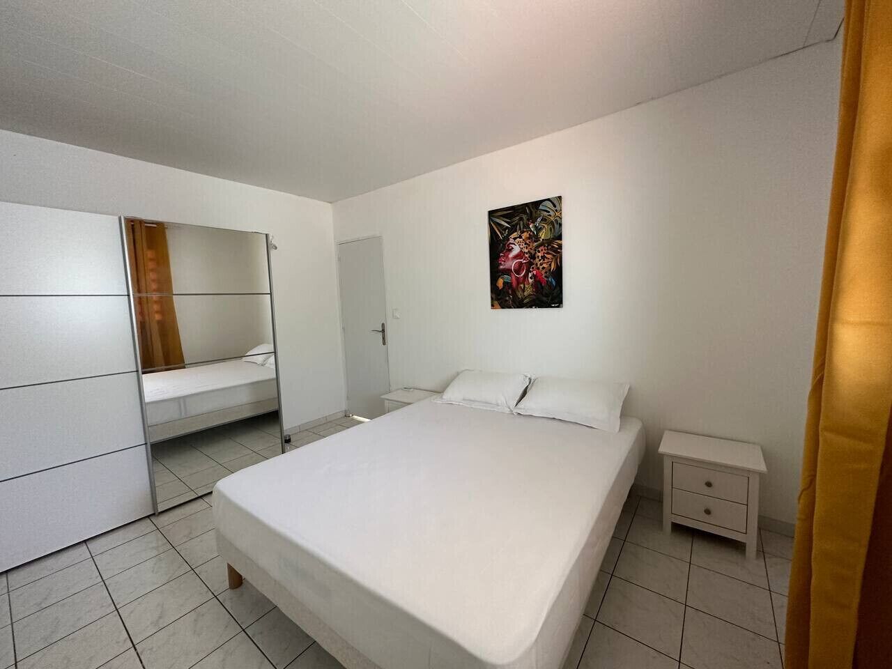 A bedroom with a large bed, a wardrobe, a bedside table, and a painting on the wall.