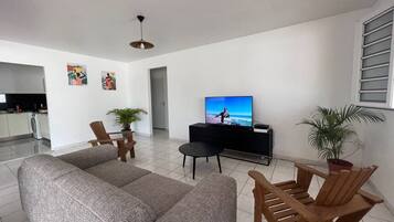 A living room with a sofa, wooden chairs, a television, and a potted plant.