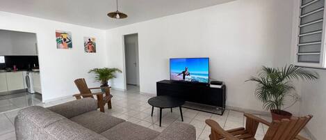 A living room with a sofa, wooden chairs, a television, and a potted plant.