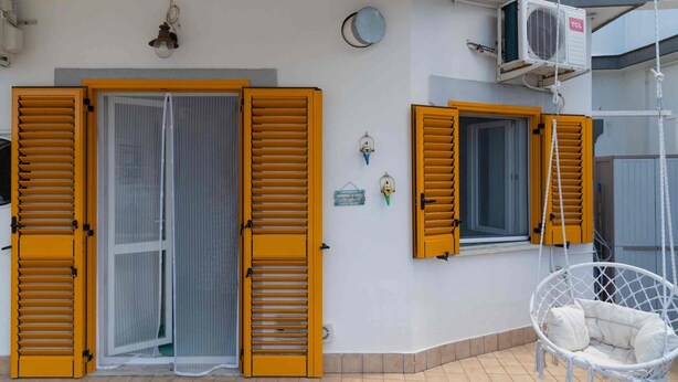Un edificio con persianas amarillas, una puerta blanca y un sillón colgante.