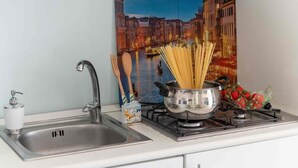 Una cocina con un lavamanos, grifo y una estufa con una olla de espagueti y un ramo de fresas.