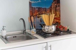 Eine Küche mit Spüle, Wasserhahn und Herd, auf dem ein Topf Spaghetti sowie eine Erdbeerschorps stehen.