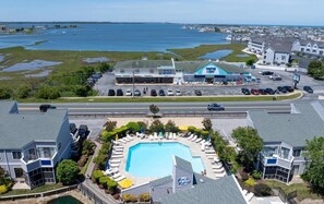 A residential area with a large swimming pool surrounded by lounge chairs and umbrellas, a parking lot, and a view of the sea. - East of the Sun - 39916 E Sun Dr #426 (Fenwick Island)