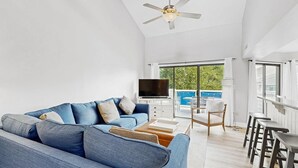 A modern living room with a blue sofa, a flat-screen TV, and a balcony with a view. - East of the Sun - 39916 E Sun Dr #426 (Fenwick Island)