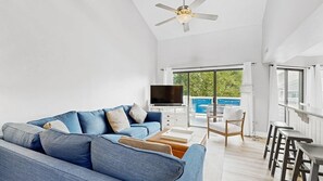 A modern living room with a blue sofa, a flat-screen TV, and a balcony with a view. - East of the Sun - 39916 E Sun Dr #426 (Fenwick Island)