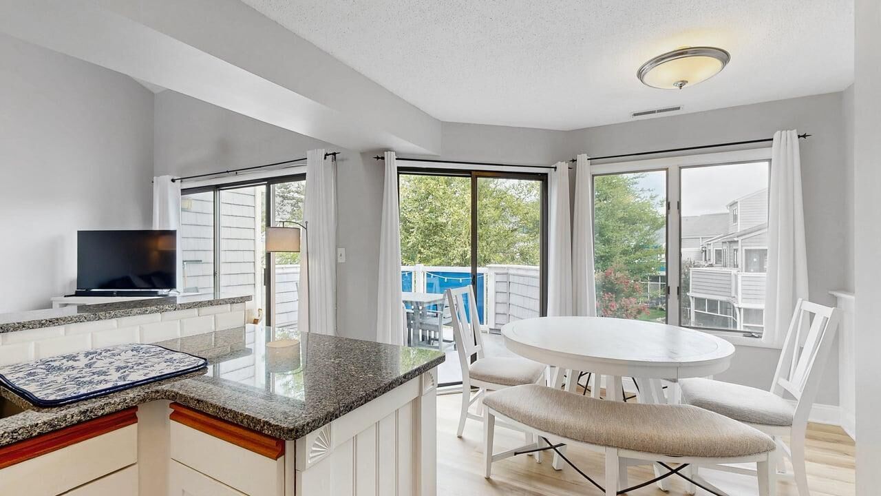 A modern kitchen with a dining area, large windows, and a flat-screen TV.