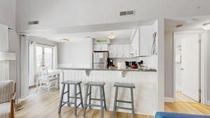 A modern kitchen with white cabinetry, a central island with stools, and a view to the dining area. - East of the Sun - 39916 E Sun Dr #426 (Fenwick Island)