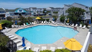A swimming pool with lounge chairs and umbrellas, surrounded by a fence, with buildings in the background. - East of the Sun - 39916 E Sun Dr #426 (Fenwick Island)