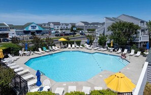 A swimming pool with lounge chairs and umbrellas, surrounded by a fence, with buildings in the background. - East of the Sun - 39916 E Sun Dr #426 (Fenwick Island)