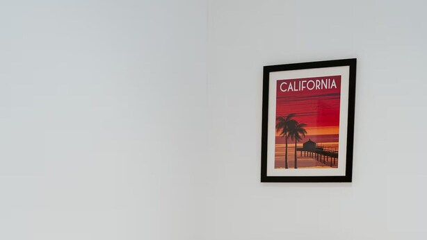 A single bed with a white mattress, a beige headboard, and a yellow pillow. A framed picture of a sunset with palm trees and a pier is on the wall. - 3 Nottingham Apts + Castle Views & City Centre (Nottingham)