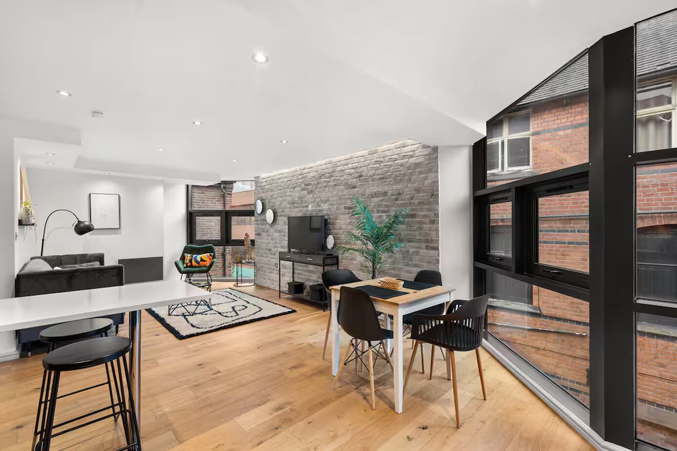A modern living space with a dining area, a sofa, a TV, and a brick wall.