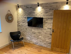 A room with a brick wall, a mounted television, a wooden door, and a black chair. - 3 Nottingham Apts + Castle Views & City Centre (Nottingham)