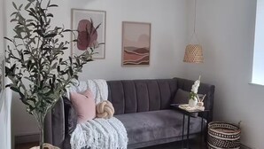 A modern living room with a grey sofa, a woven chair, a small table with decorative items, and a potted plant. - 3 Nottingham Apts + Castle Views & City Centre (Nottingham)