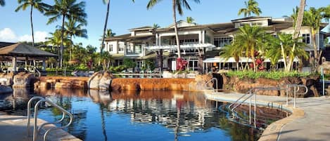 A resort with a swimming pool, palm trees, and a building with multiple balconies.