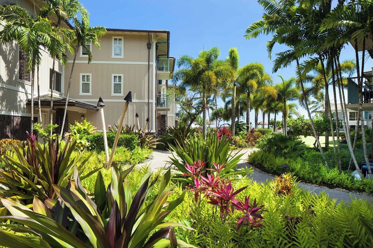 A hotel with a two-story building, a landscaped garden with tropical plants, and a clear sky.