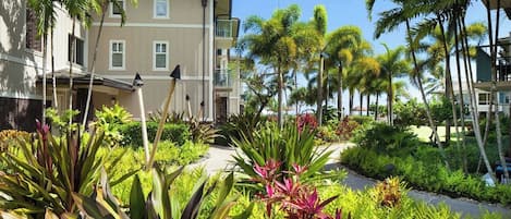 A hotel with a two-story building, a landscaped garden with tropical plants, and a clear sky.
