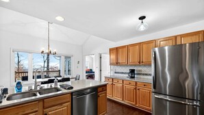 A modern kitchen with wooden cabinets, stainless steel appliances, and a large window overlooking a deck. - Stunning Hedgesville Mountain Home with Fire Pit & Screened Porch Near Hedgesville, WV (Hedgesville)