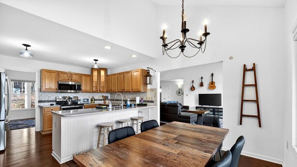 A modern kitchen with wooden cabinets, a central island, and a dining area with a large wooden table. - Stunning Hedgesville Mountain Home with Fire Pit & Screened Porch Near Hedgesville, WV (Hedgesville)