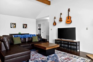 Ein Wohnzimmer mit braunem Ledersofa, einem Holztisch, einem Flachbildfernseher und einer Wandvitrine mit Gitarren.