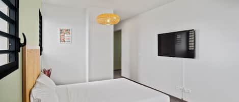 A bedroom with a bed, a television mounted on the wall, and a hanging light fixture.