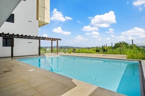 Ein Pool mit einer Pergola, ein weißes Gebäude und ein klarer Himmel.