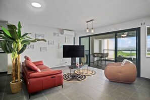 Ein modernes Wohnzimmer mit einem roten Sofa, einem Fernseher, einem Couchtisch und einer großen Topfpflanze.