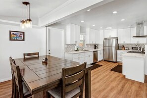 A modern kitchen with white cabinets, stainless steel appliances, and a wooden dining table. - Charming Cottage with Foosball and Hot-tub in Big Bear Lake, California (Big Bear Lake)