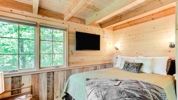 Een slaapkamer in een houten chalet met een bed, een wandtelevisie en een raam met uitzicht op bomen.