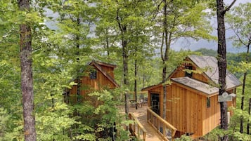 A cabin with a deck and a small porch, surrounded by trees.