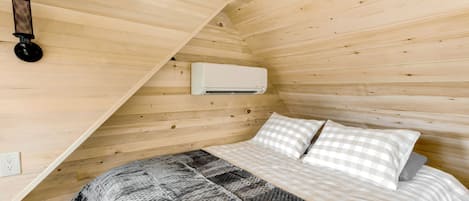 A wooden cabin room with a bed, a checkered blanket, and a wall-mounted air conditioner.