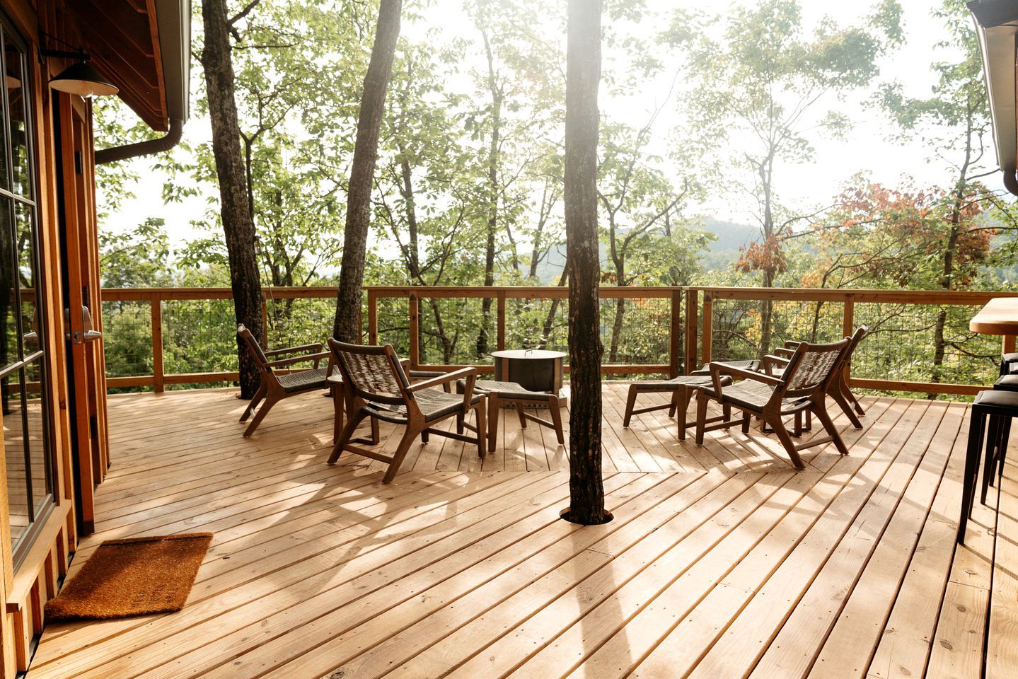 A wooden deck with outdoor furniture, a small table, and a view of trees and mountains.