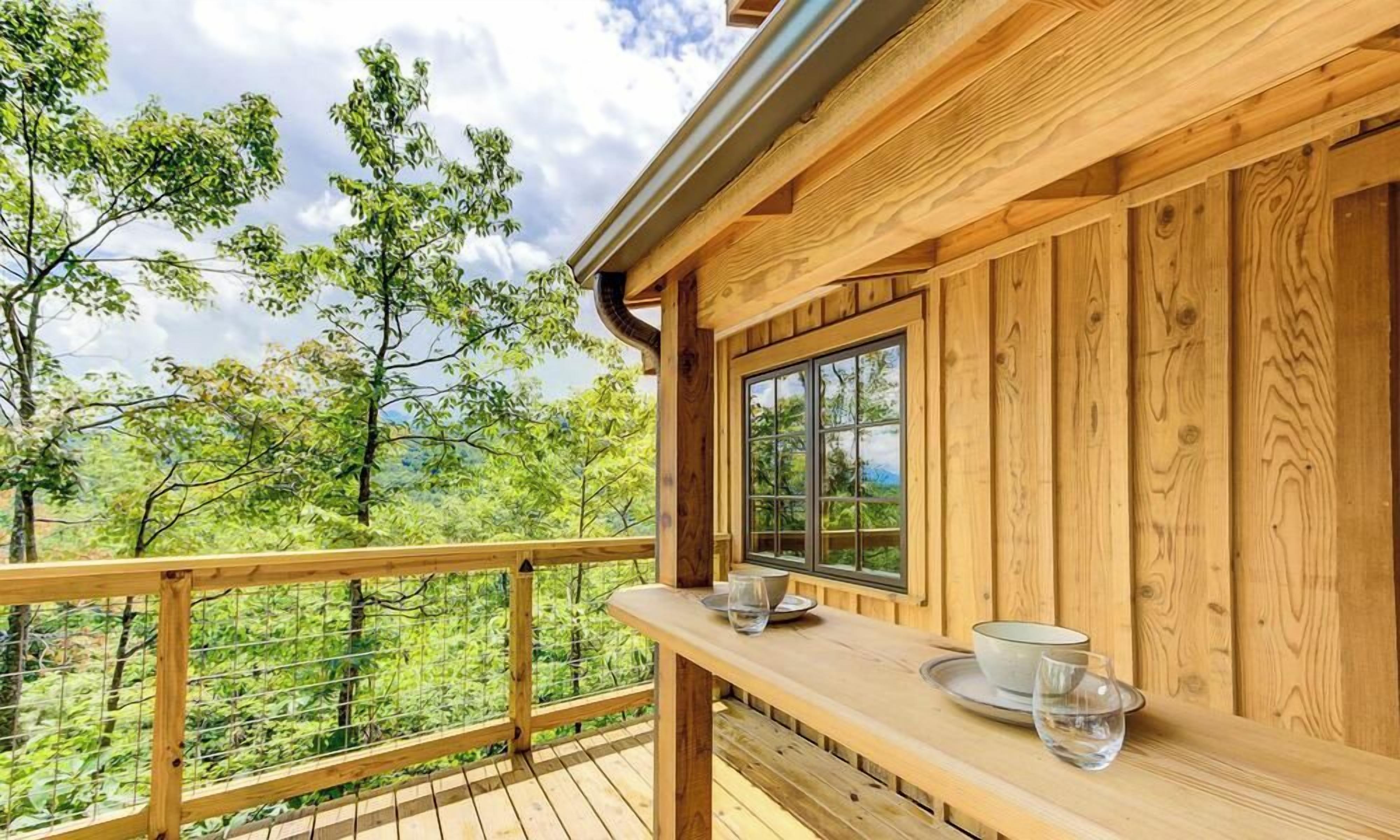 A wooden deck with a table and chairs, overlooking a forested area.