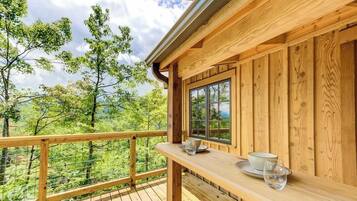 A wooden deck with a table and chairs, overlooking a forested area.