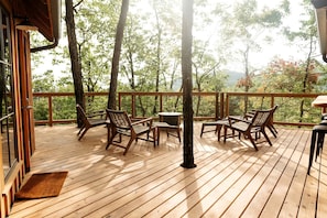 A wooden deck with outdoor furniture, a small table, and a view of trees and mountains. - Impressive Tree House with Barbecue and Hot-tub in Gatlinburg, Tennessee (Gatlinburg)
