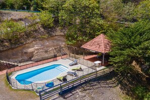 Ein Schwimmbad mit umzäuntem Deck, Liegestühlen und einem Pavillon.