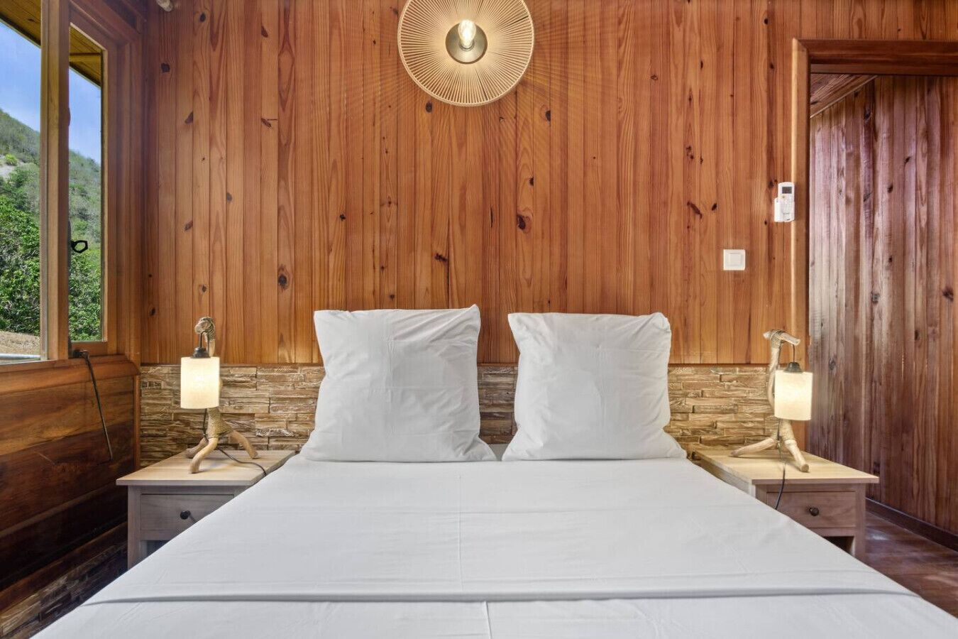 A wooden-paneled bedroom with a bed, two bedside lamps, and a wall-mounted light fixture.