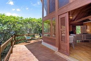 A wooden deck with outdoor furniture, a large window, and a view of the surrounding trees. - Chalet Jujube - Beautiful cottage with a pool (Les Anses-d`Arlet)