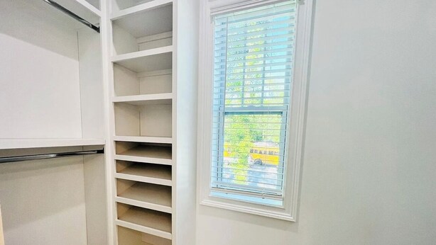 Quarto com roupeiro embutido, com diversas prateleiras e janela com persianas.