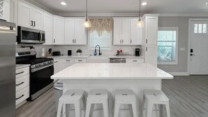Uma cozinha moderna com armários brancos, eletrodomésticos de aço inoxidável e uma ilha central com banquetas.