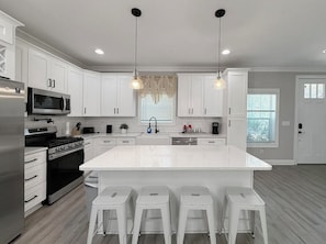 Una cocina moderna con armarios blancos, electrodomésticos de acero inoxidable y una isla central con taburetes de bar.