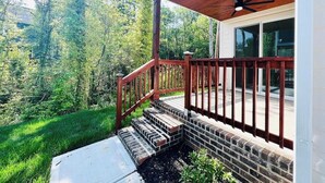 Um deck de madeira com uma escadaria de tijolos que leva a uma casa com porta de vidro.