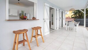 A modern kitchen with white cabinets, a wooden bar stool, and a hanging light fixture. - Villa Kaliemma - Tropical Villa in Martinique (Le Marin)